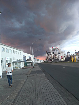 Rega spaziert auf der Werftstraße unter drohenden Himmelsfarben, Häuser und Schiffe
